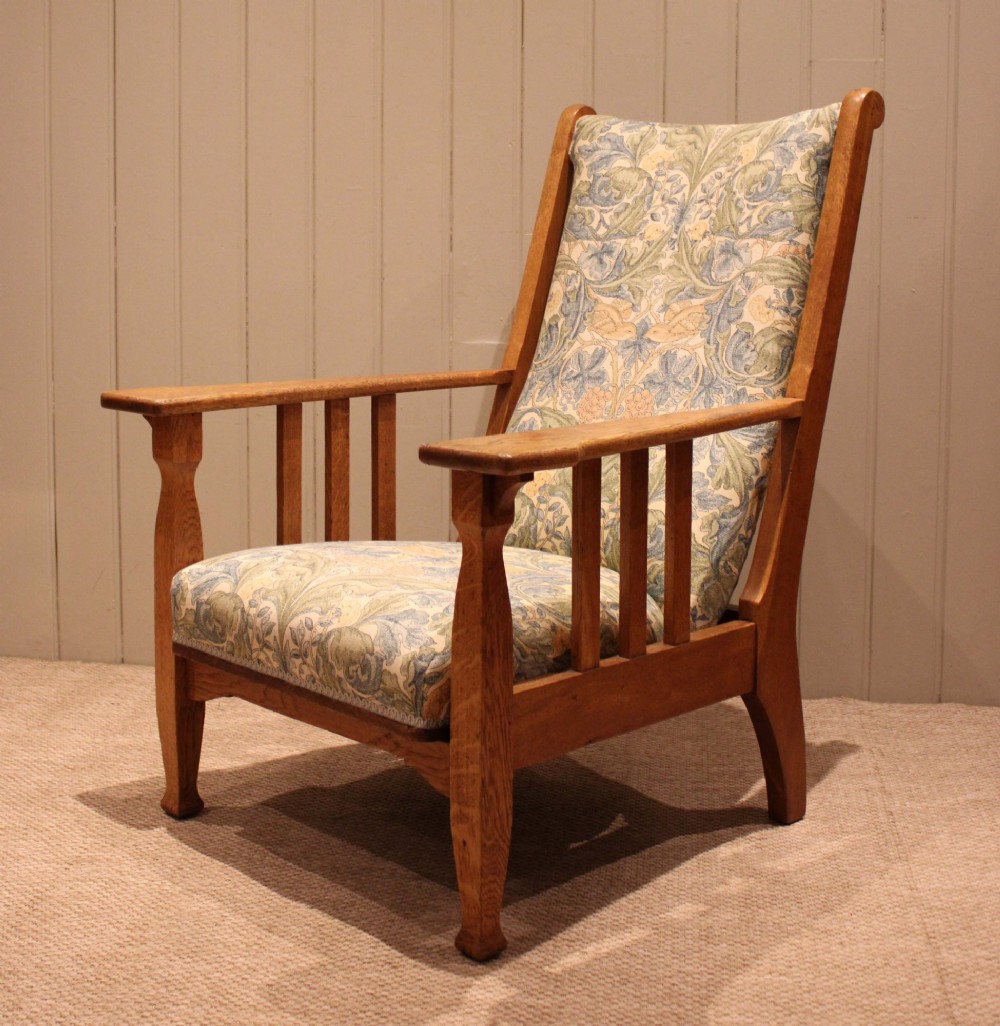 A solid oak Arts and Crafts style armchair featuring broad flat armrests and upholstery decorated with a botanical foliage pattern. View V