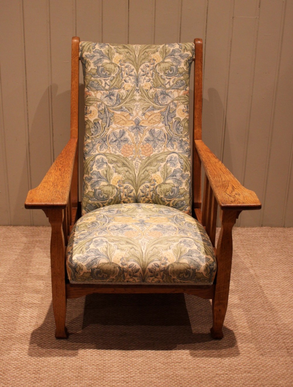 A solid oak Arts and Crafts style armchair featuring broad flat armrests and upholstery decorated with a botanical foliage pattern. View VI