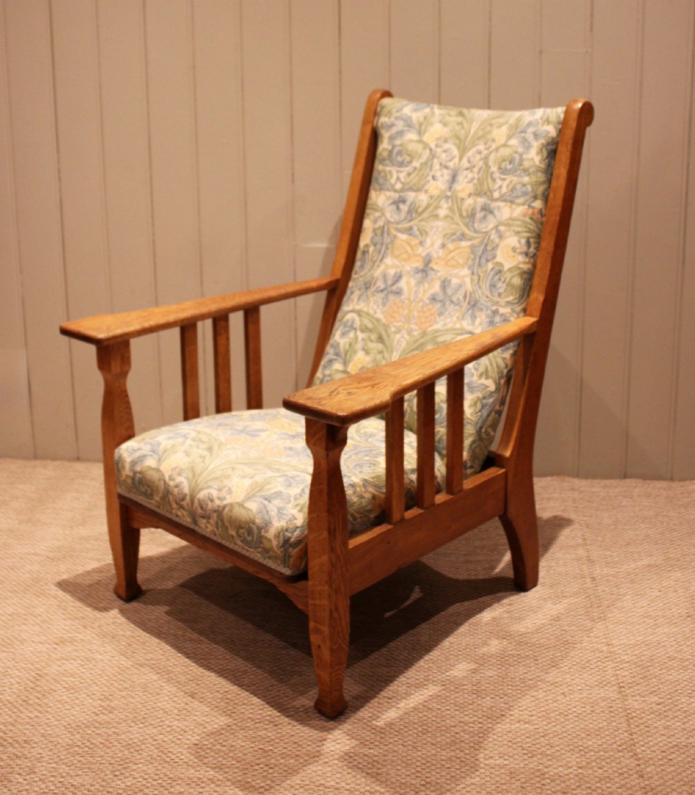 A solid oak Arts and Crafts style armchair featuring broad flat armrests and upholstery decorated with a botanical foliage pattern. View VII