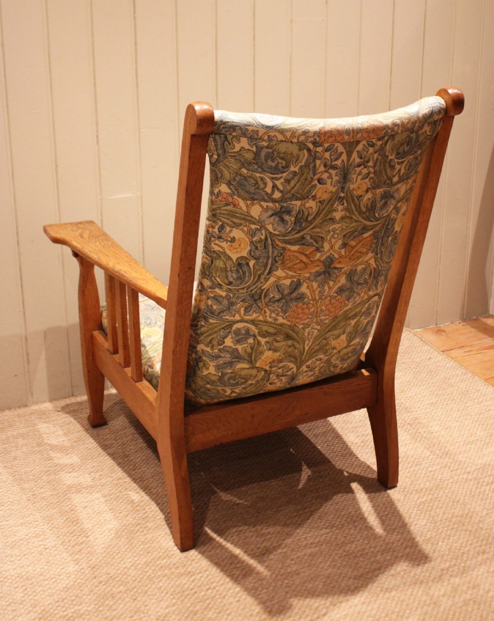A solid oak Arts and Crafts style armchair featuring broad flat armrests and upholstery decorated with a botanical foliage pattern. View VIII