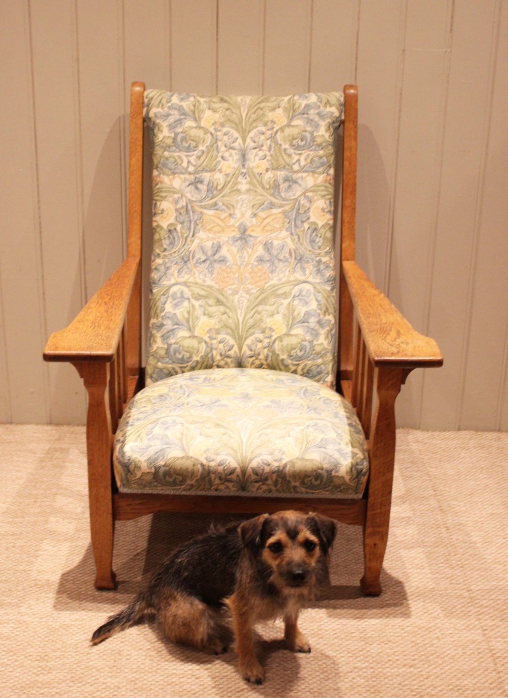 A solid oak Arts and Crafts style armchair featuring broad flat armrests and upholstery decorated with a botanical foliage pattern. View X