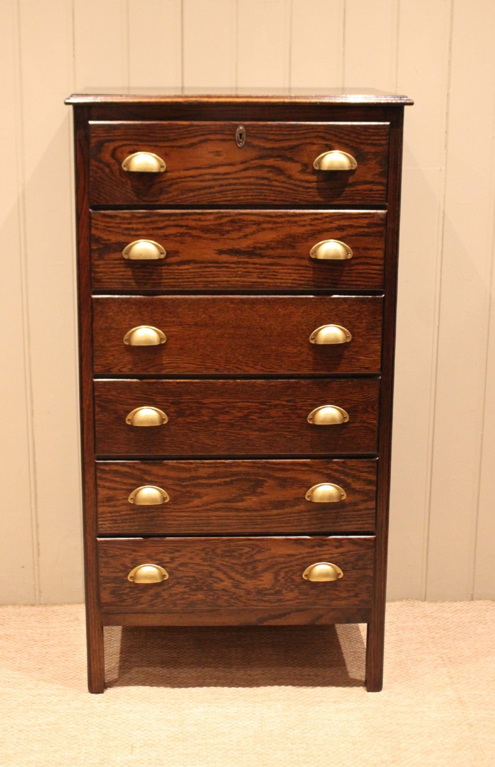 A tall dark oak chest with six stacked drawers and brass cup handles. View II