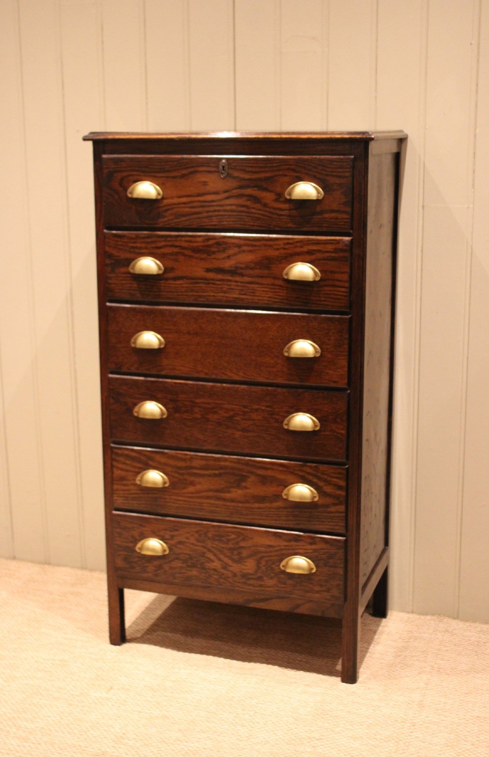 A tall dark oak chest with six stacked drawers and brass cup handles. View III