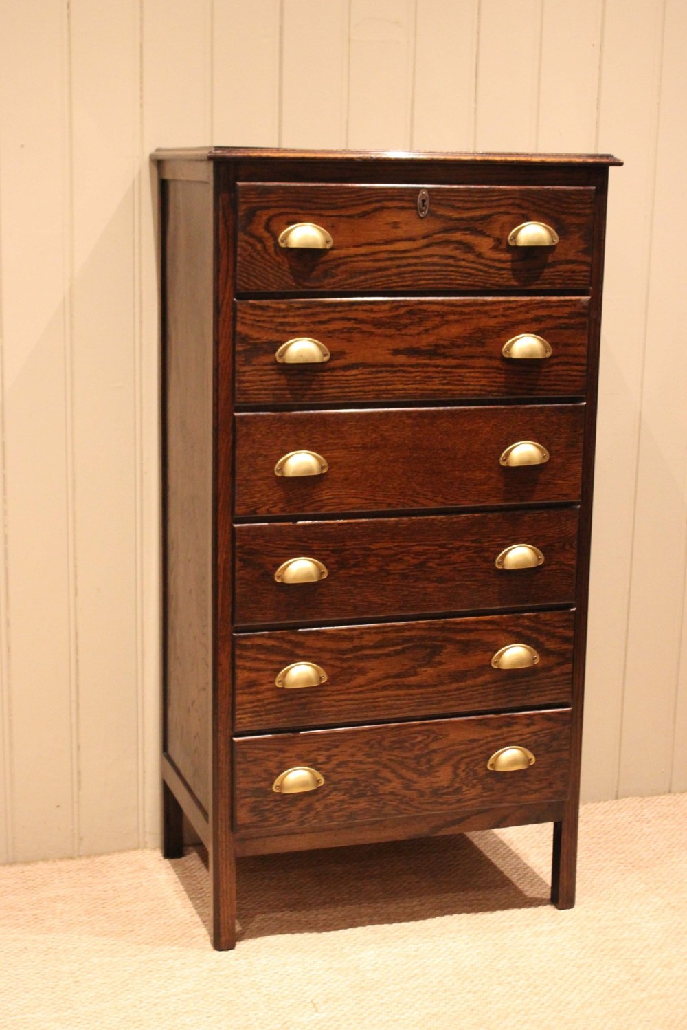 A tall dark oak chest with six stacked drawers and brass cup handles. View IV
