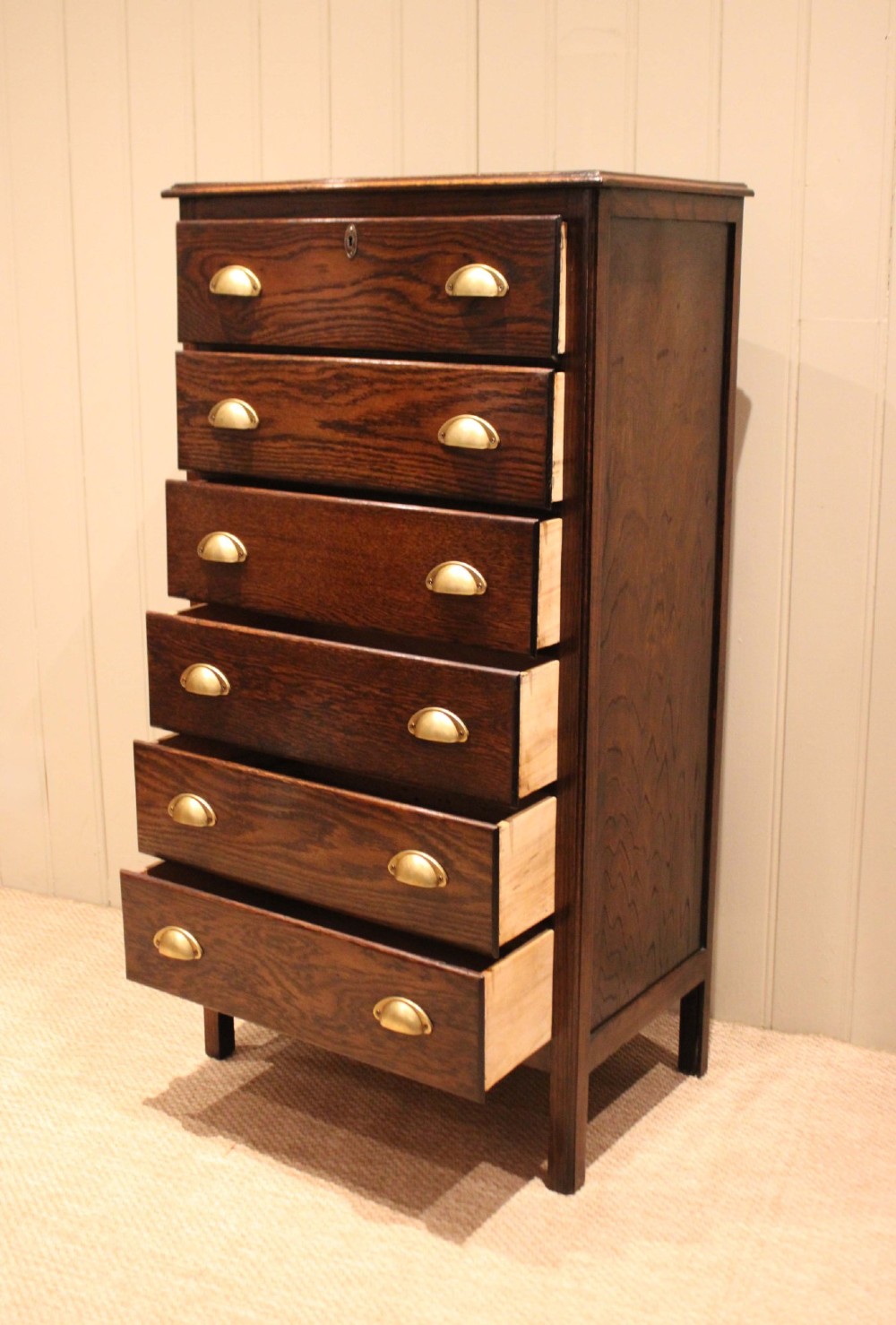 A tall dark oak chest with six stacked drawers and brass cup handles. View V