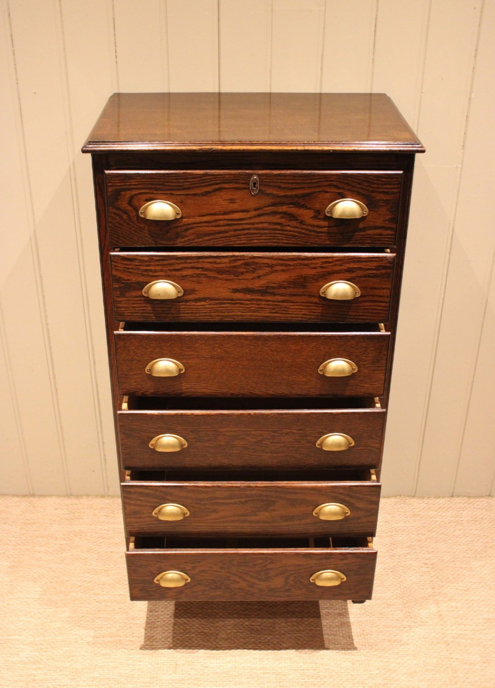 A tall dark oak chest with six stacked drawers and brass cup handles. View VI