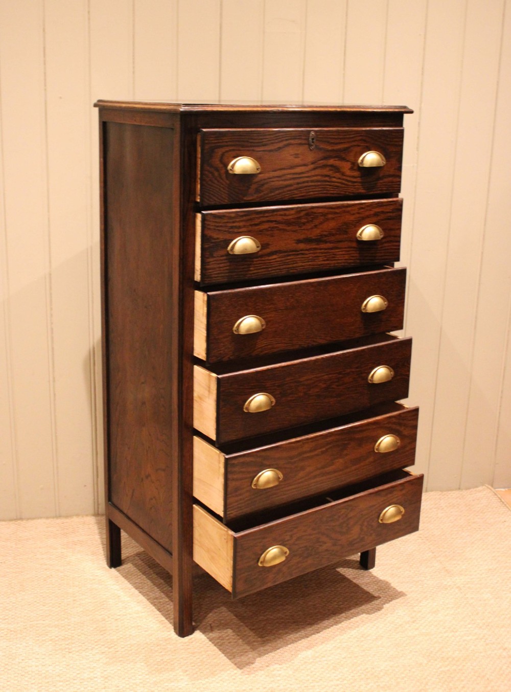 A tall dark oak chest with six stacked drawers and brass cup handles. View VII