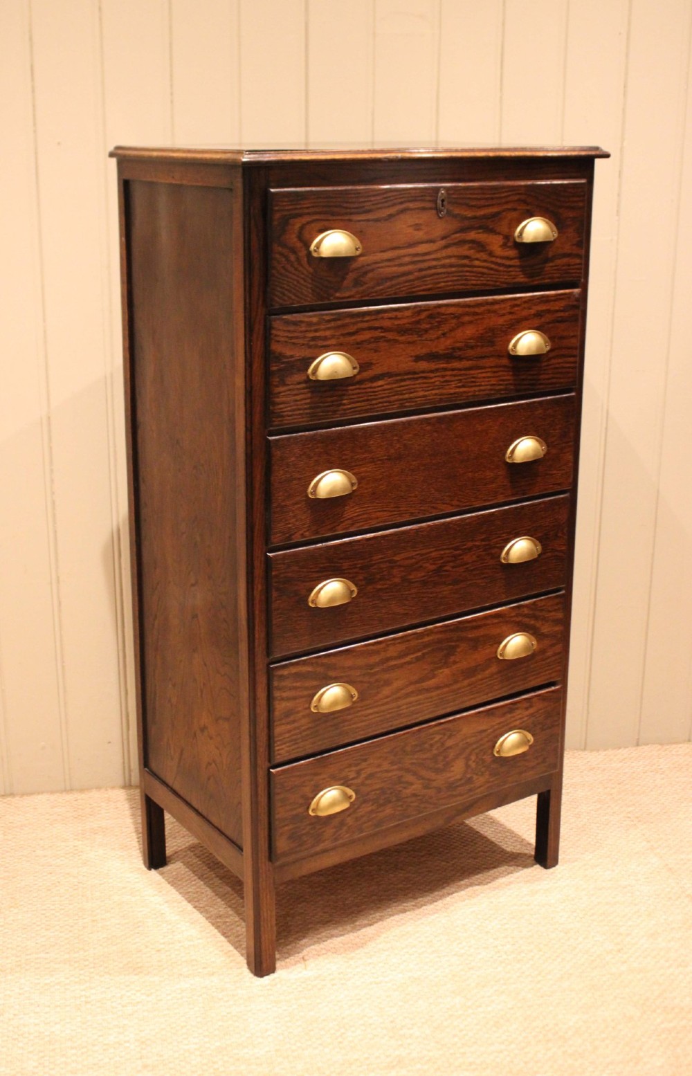 A tall dark oak chest with six stacked drawers and brass cup handles. View VIII