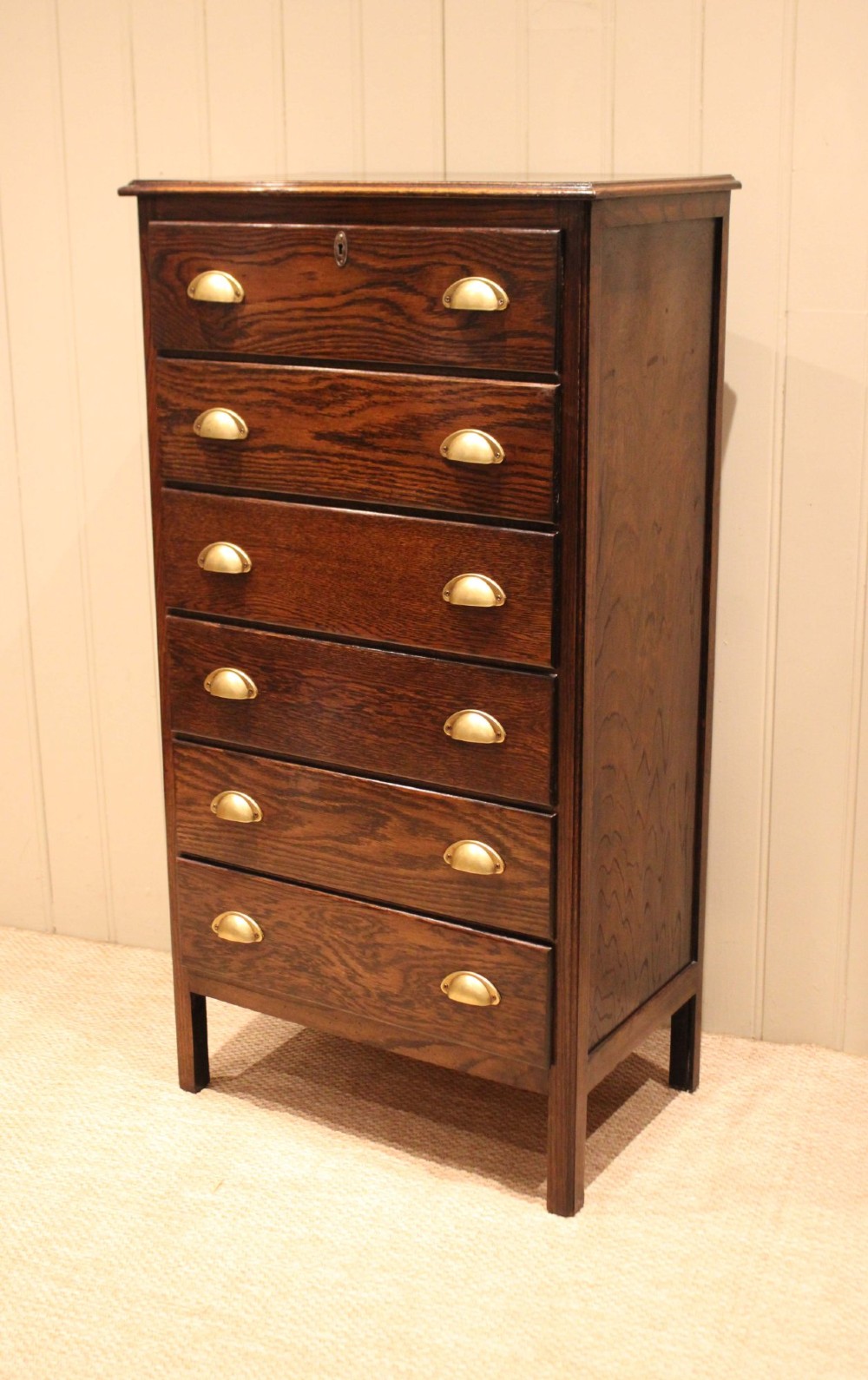 A tall dark oak chest with six stacked drawers and brass cup handles. View IX
