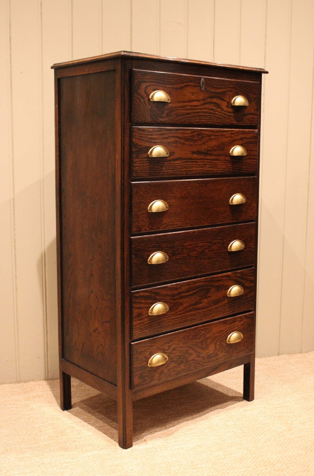 A tall dark oak chest with six stacked drawers and brass cup handles. View XI