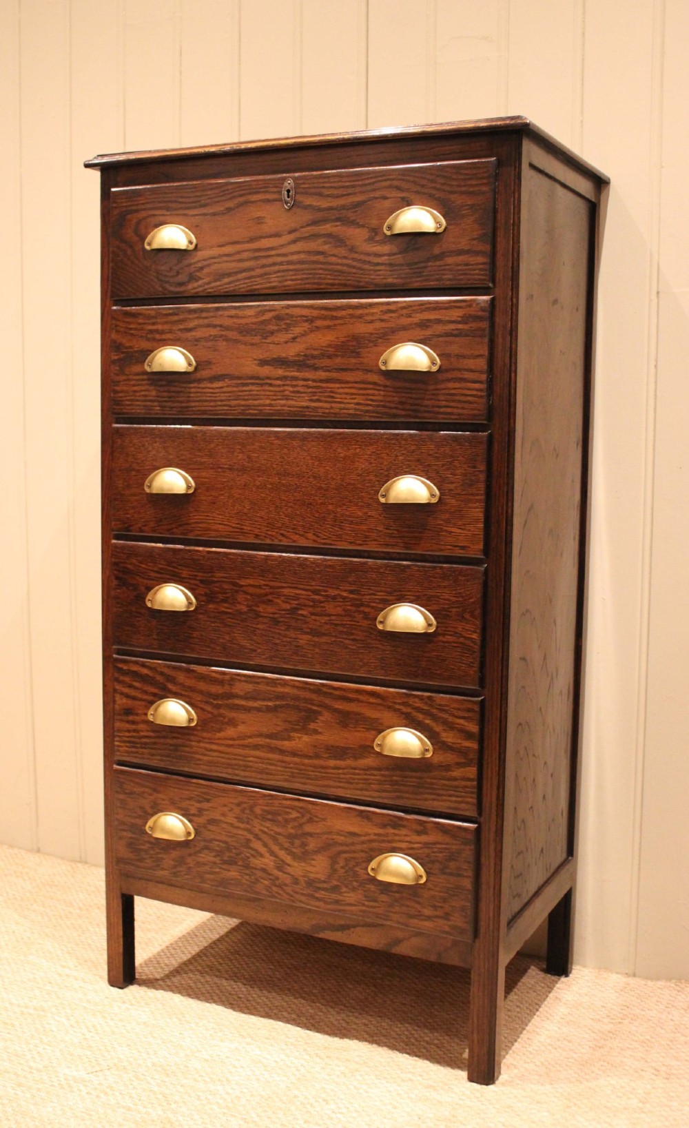 A tall dark oak chest with six stacked drawers and brass cup handles. View XII