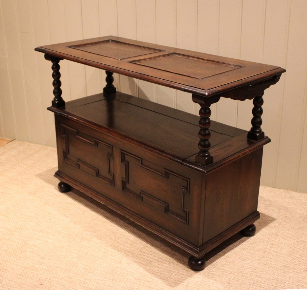 A dark oak monks bench with geometric moulded panels on the backrest and storage base, supported by turned posts and bun feet. View VIII