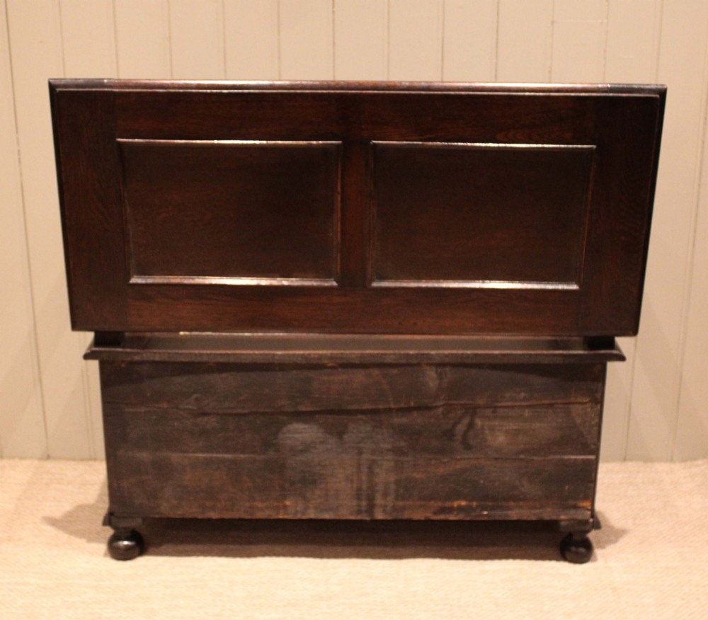 A dark oak monks bench with geometric moulded panels on the backrest and storage base, supported by turned posts and bun feet. View XII