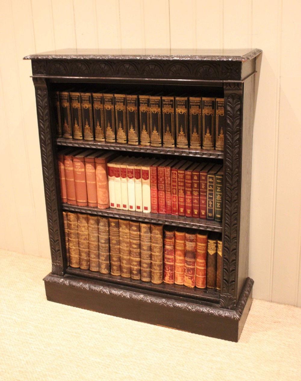 A mid-Victorian dark oak open bookcase featuring hand-carved leaf mouldings and three open shelves filled with antique books.