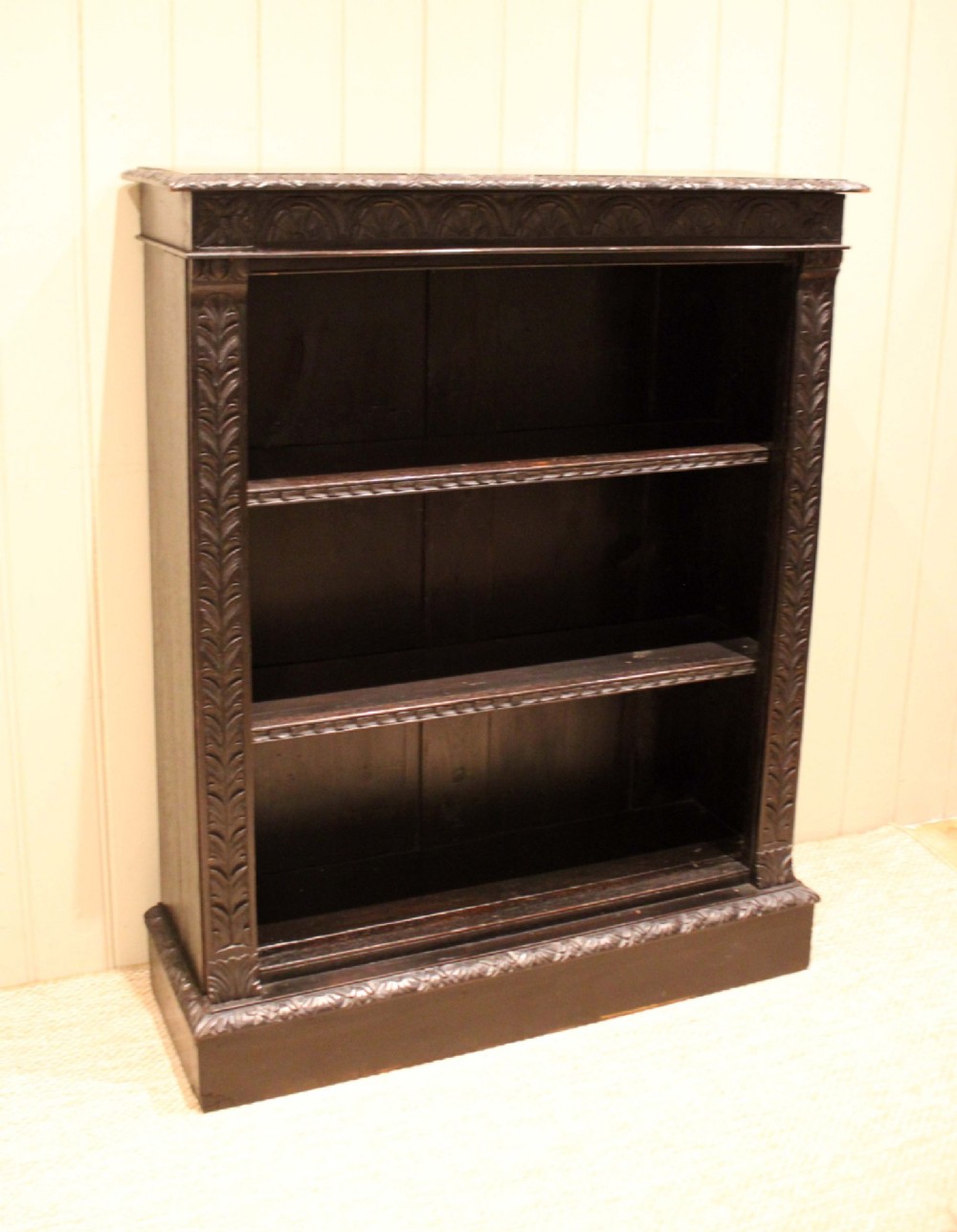 A mid-Victorian dark oak open bookcase featuring hand-carved leaf mouldings and three open shelves filled with antique books. View II
