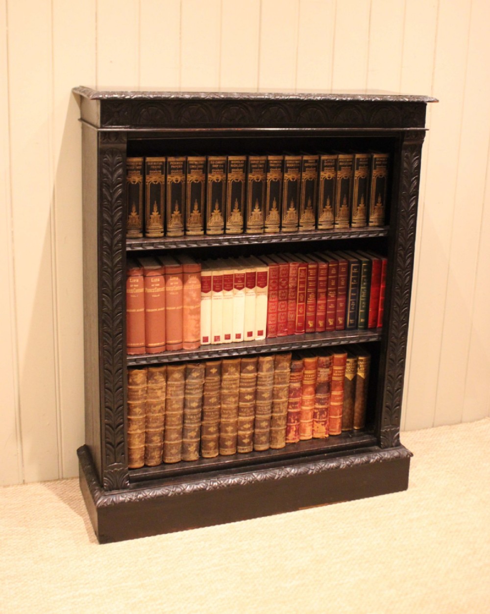 A mid-Victorian dark oak open bookcase featuring hand-carved leaf mouldings and three open shelves filled with antique books. View III