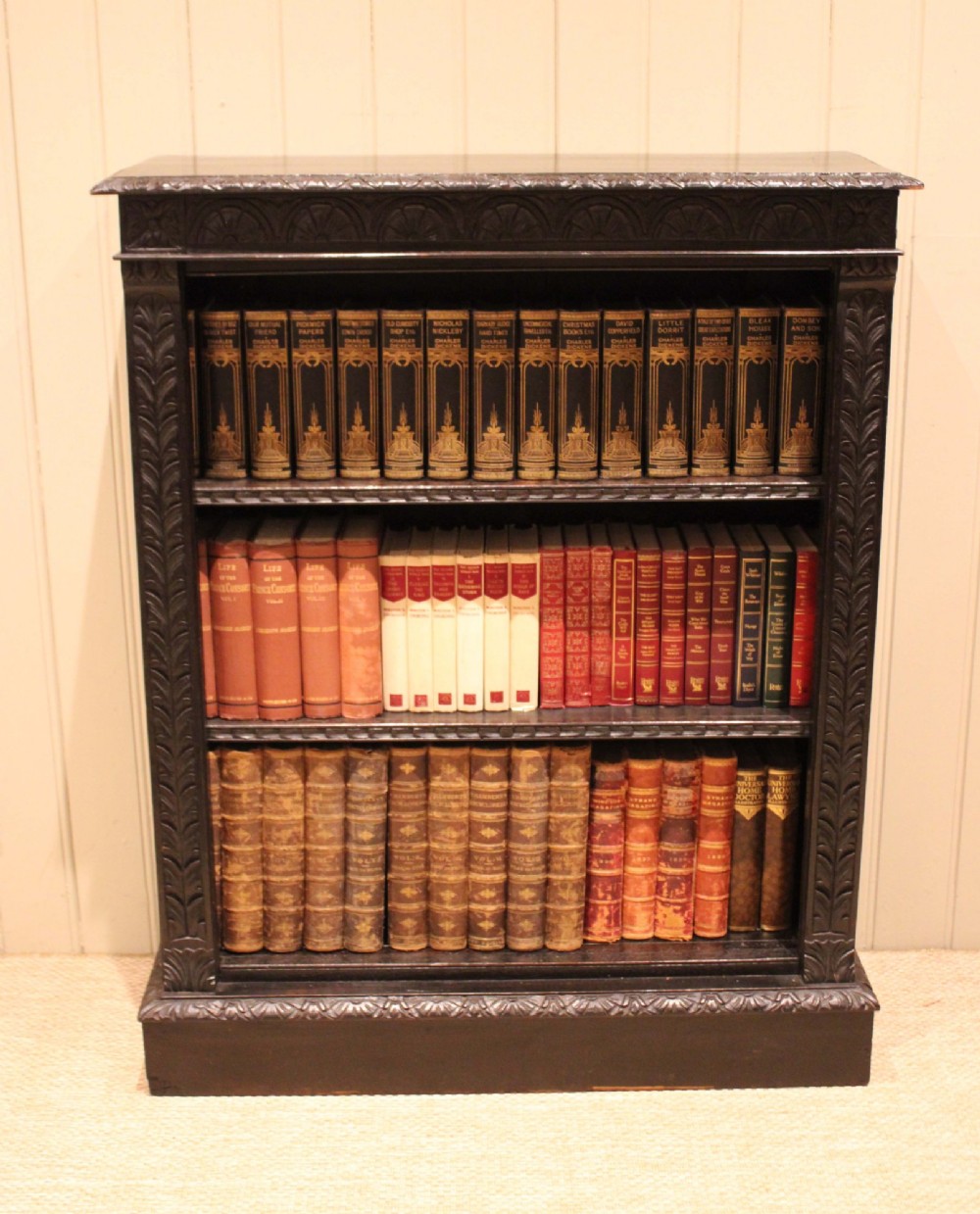 A mid-Victorian dark oak open bookcase featuring hand-carved leaf mouldings and three open shelves filled with antique books. View V