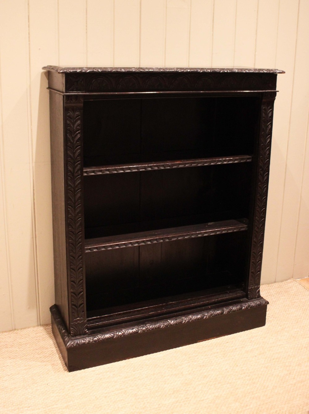 A mid-Victorian dark oak open bookcase featuring hand-carved leaf mouldings and three open shelves filled with antique books. View VI