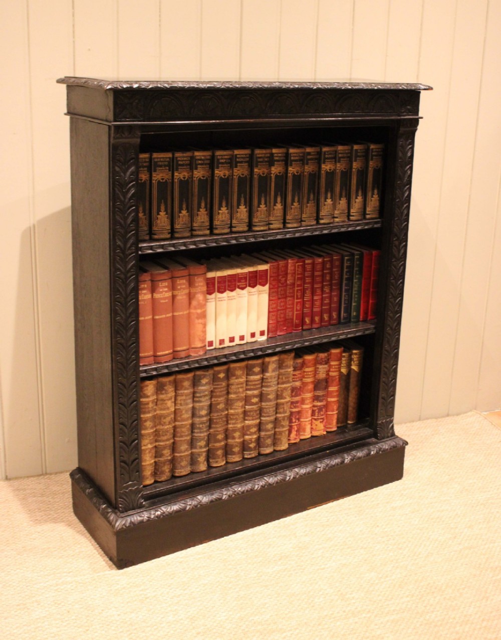 A mid-Victorian dark oak open bookcase featuring hand-carved leaf mouldings and three open shelves filled with antique books. View IX