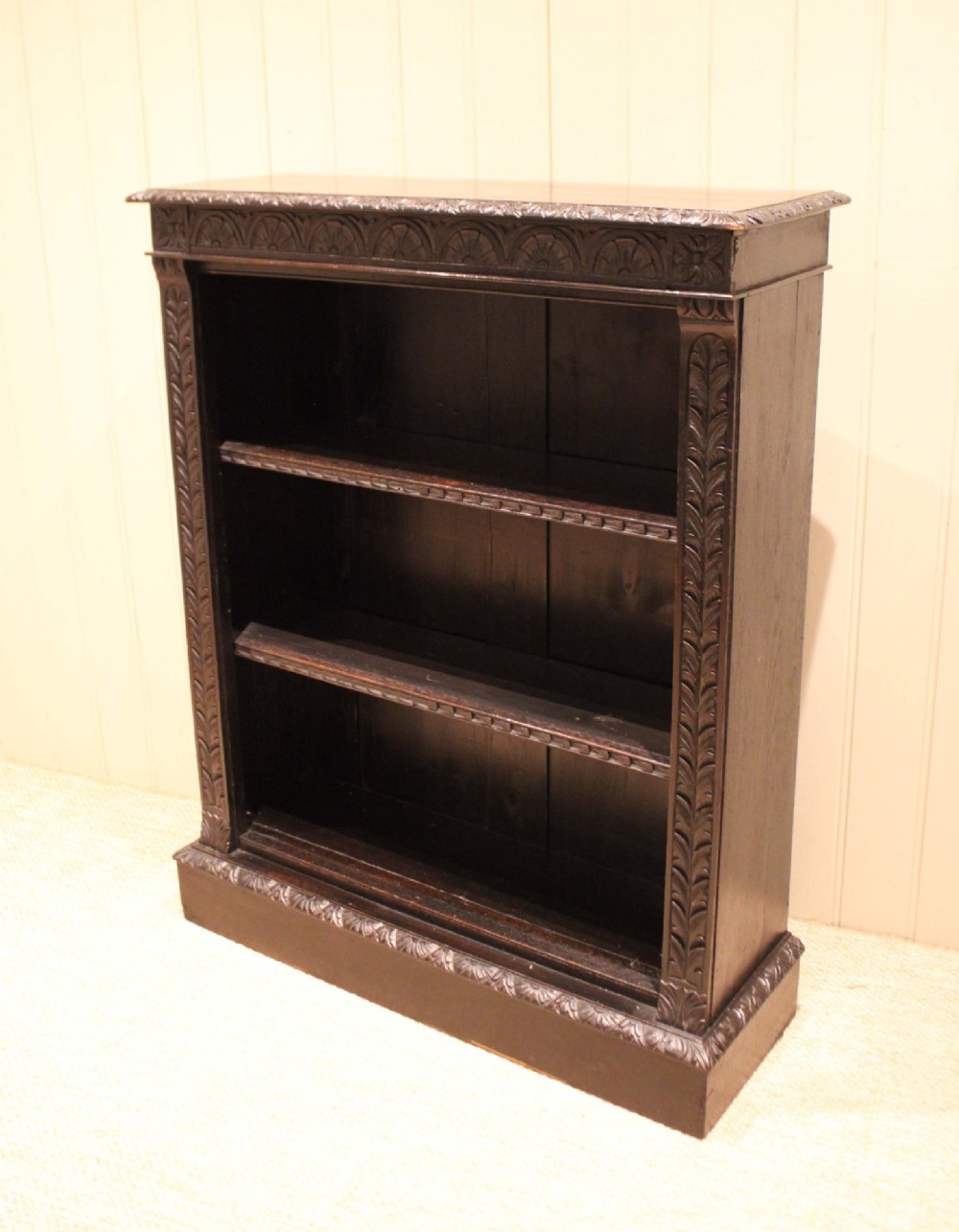 A mid-Victorian dark oak open bookcase featuring hand-carved leaf mouldings and three open shelves filled with antique books. View X