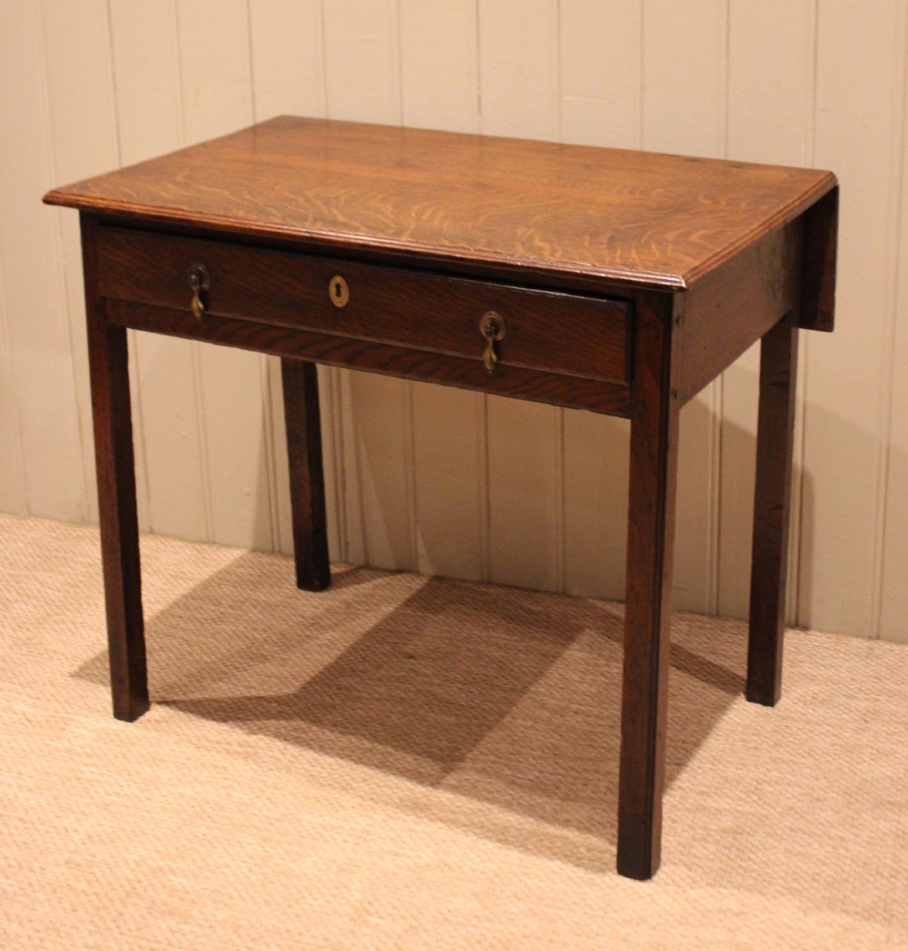 A George III oak side table with a frieze drawer, brass drop handles, a keyhole escutcheon, and straight square legs.
