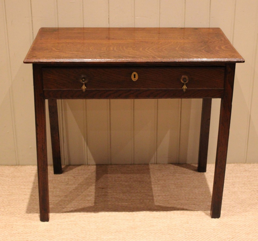 A George III oak side table with a frieze drawer, brass drop handles, a keyhole escutcheon, and straight square legs. View II