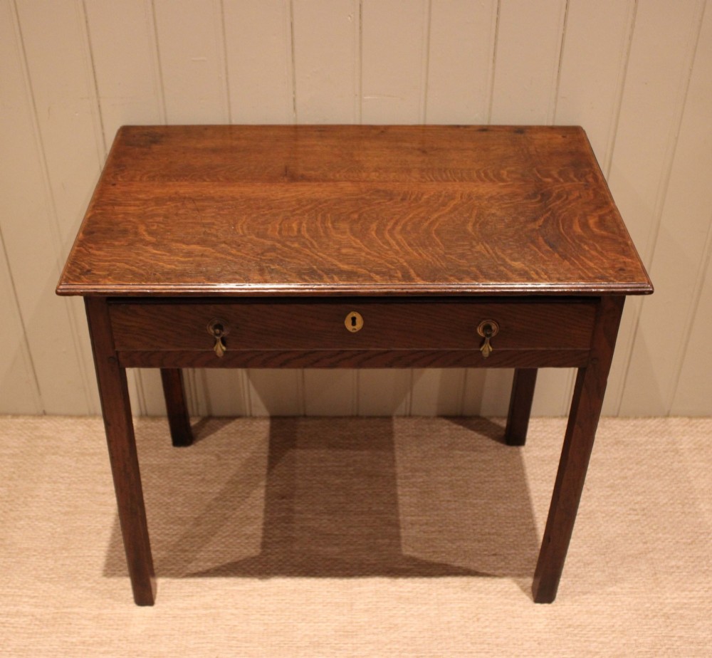 A George III oak side table with a frieze drawer, brass drop handles, a keyhole escutcheon, and straight square legs. View IV