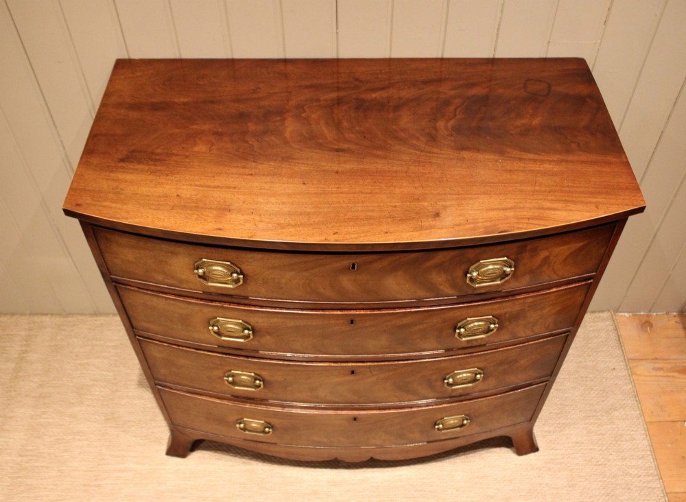 A Georgian flame mahogany bowfront chest of drawers featuring four graduated drawers with brass handles and splayed bracket feet. View VI