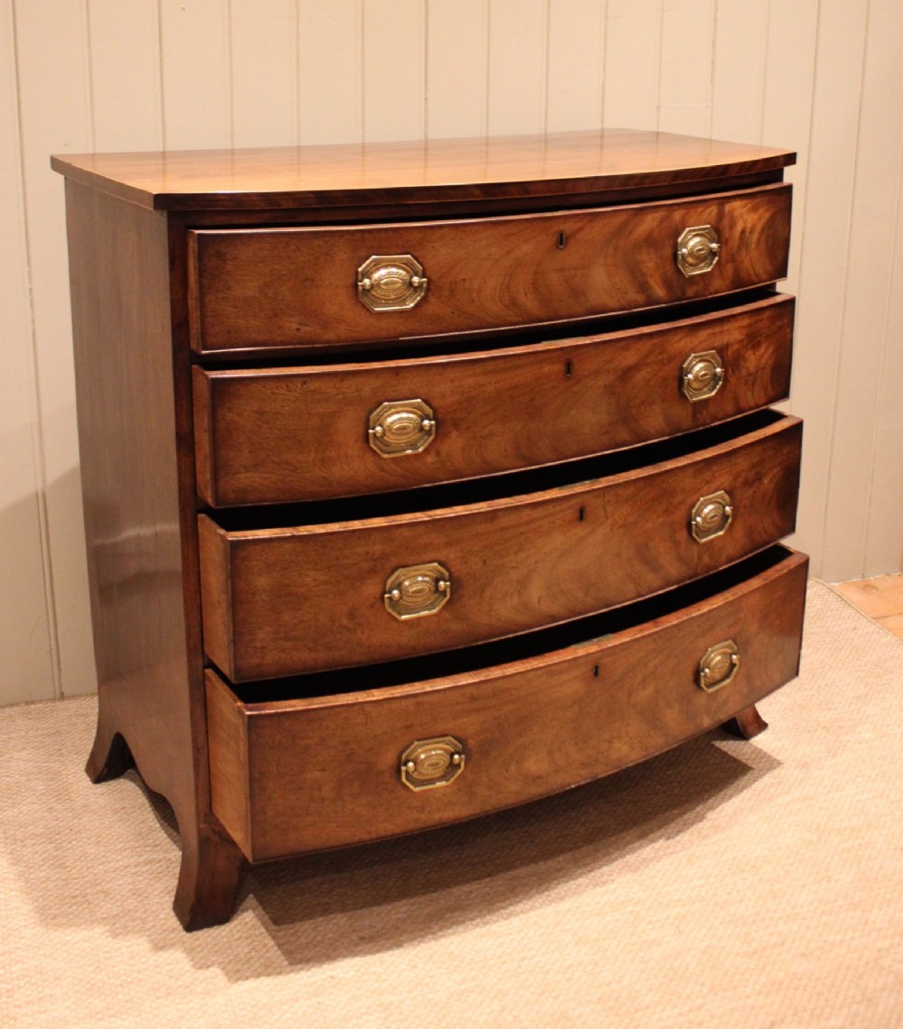 A Georgian flame mahogany bowfront chest of drawers featuring four graduated drawers with brass handles and splayed bracket feet. View X