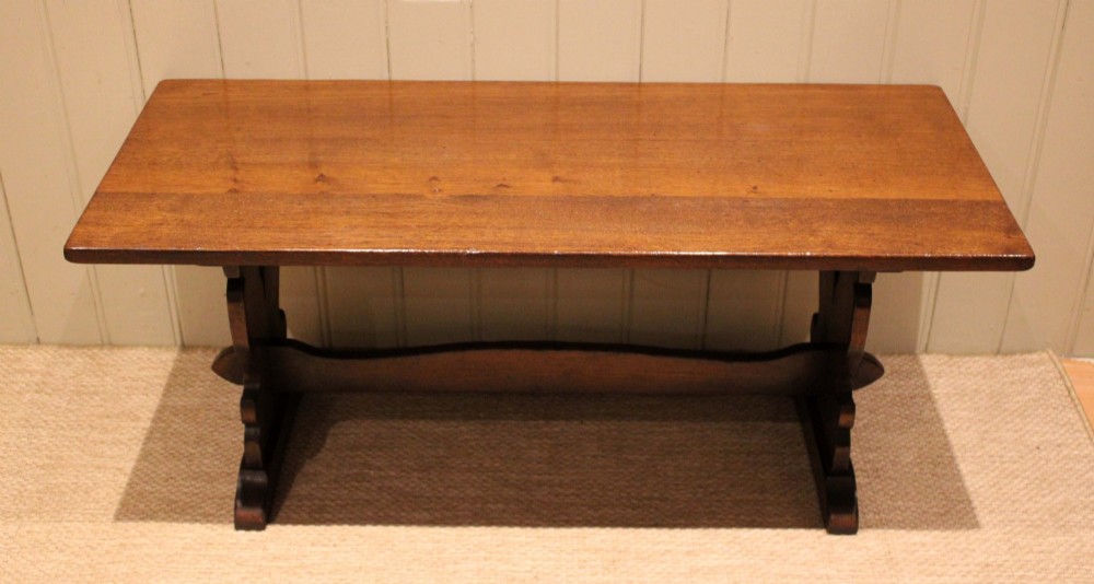 A solid oak rectangular low coffee table featuring a plain plank top set on a trestle base with shaped end supports and a single stretcher rail.