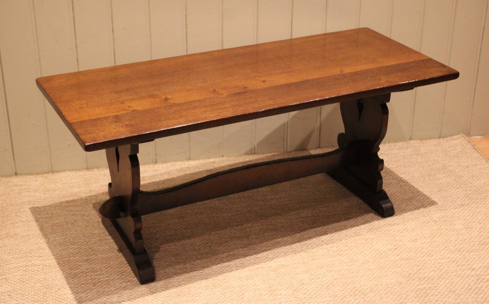 A solid oak rectangular low coffee table featuring a plain plank top set on a trestle base with shaped end supports and a single stretcher rail. View II