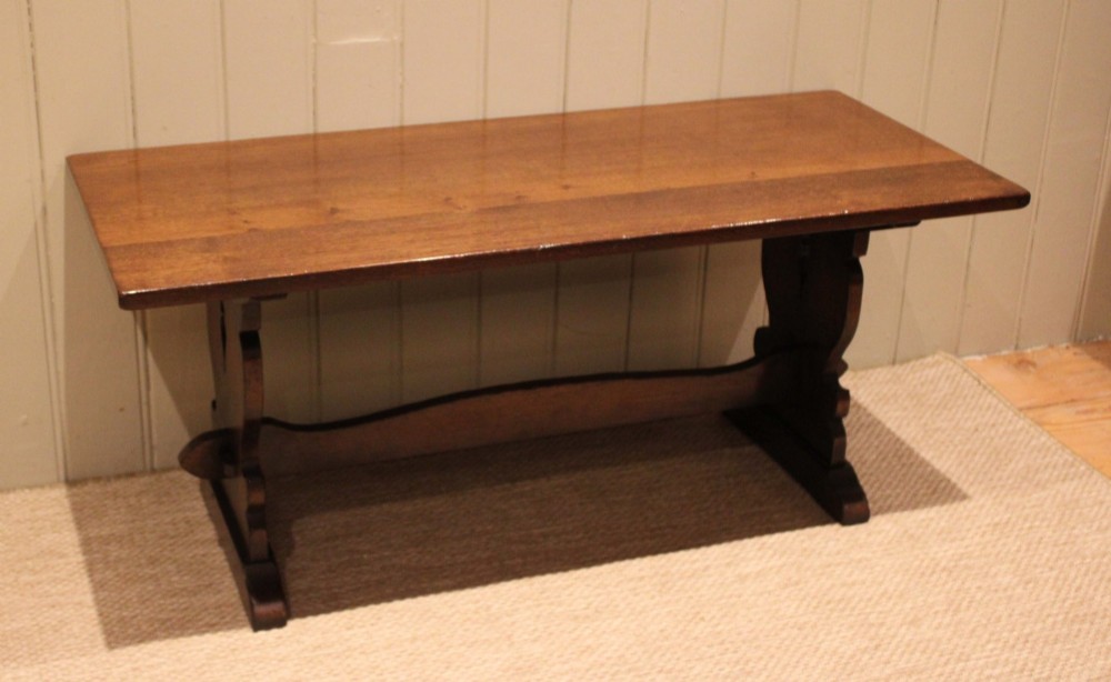 A solid oak rectangular low coffee table featuring a plain plank top set on a trestle base with shaped end supports and a single stretcher rail. View III