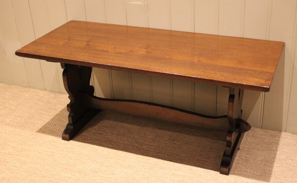 A solid oak rectangular low coffee table featuring a plain plank top set on a trestle base with shaped end supports and a single stretcher rail. View IV