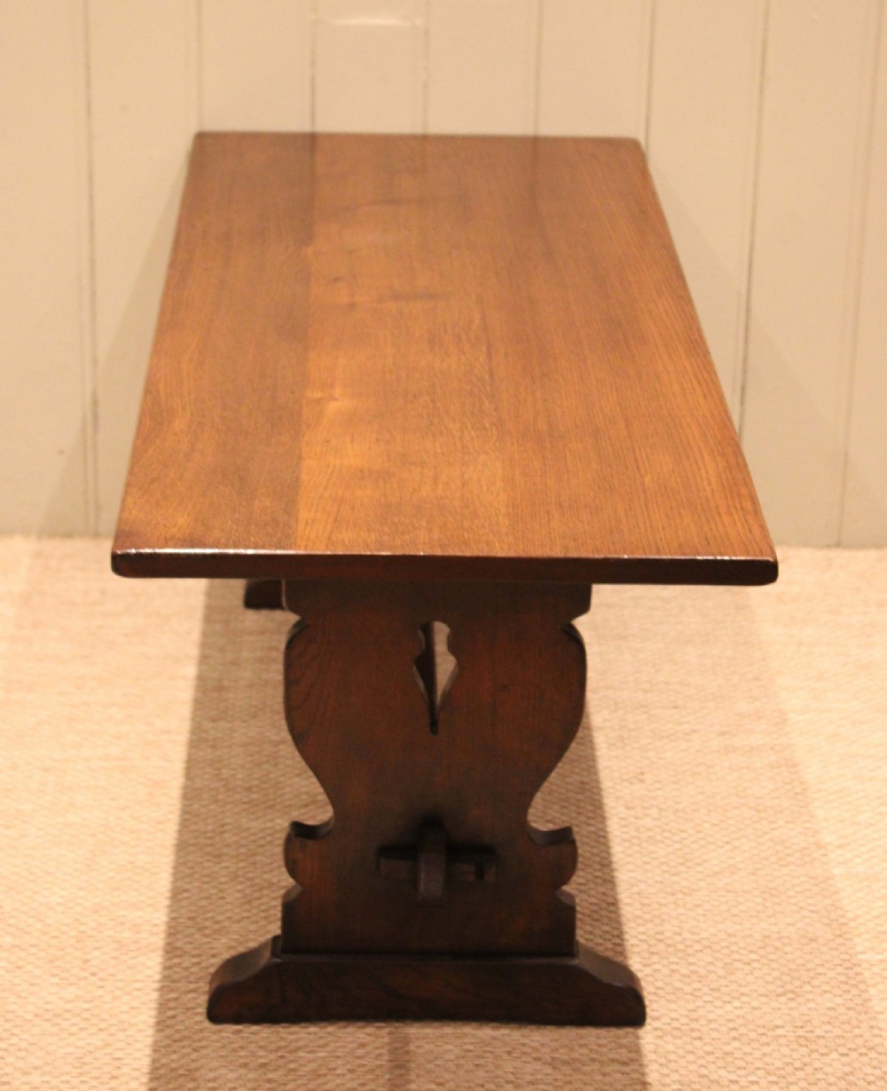 A solid oak rectangular low coffee table featuring a plain plank top set on a trestle base with shaped end supports and a single stretcher rail. View VI
