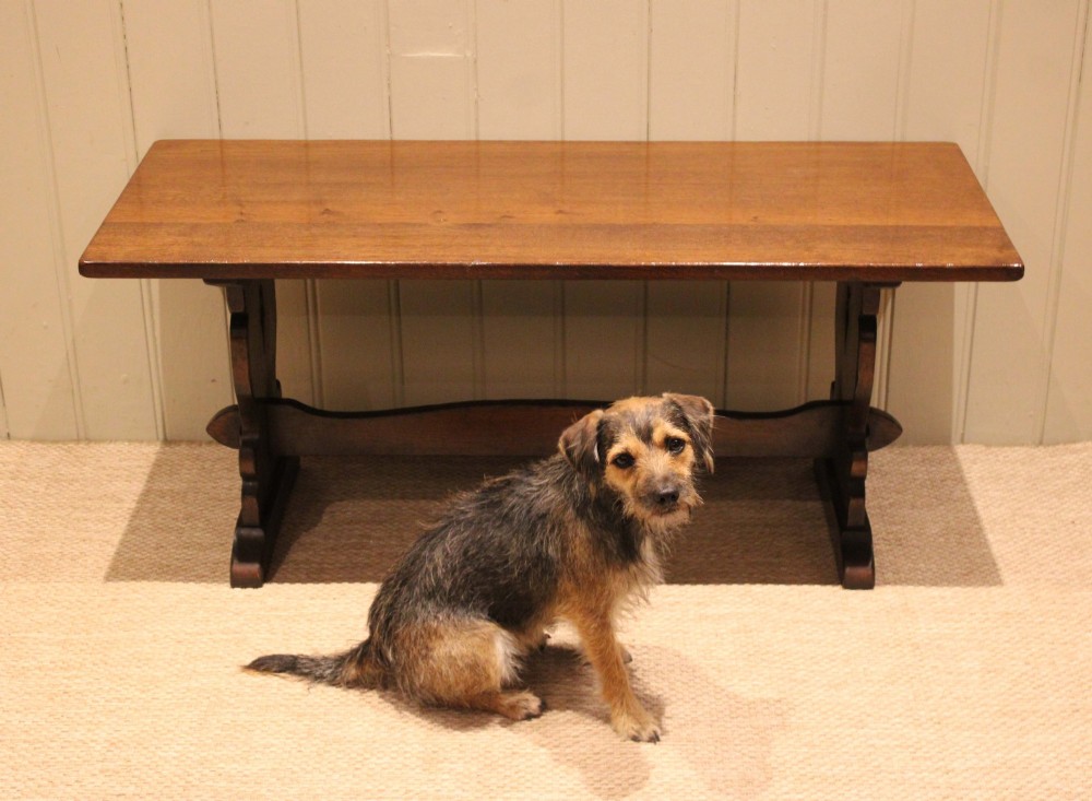 A solid oak rectangular low coffee table featuring a plain plank top set on a trestle base with shaped end supports and a single stretcher rail. View VII