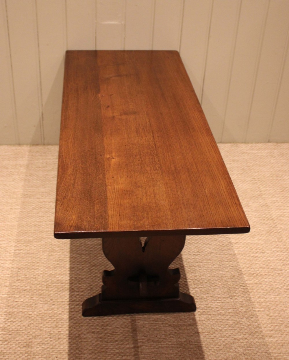 A solid oak rectangular low coffee table featuring a plain plank top set on a trestle base with shaped end supports and a single stretcher rail. View VIII
