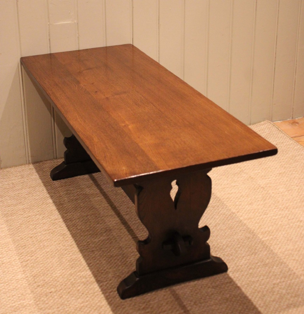 A solid oak rectangular low coffee table featuring a plain plank top set on a trestle base with shaped end supports and a single stretcher rail. View X