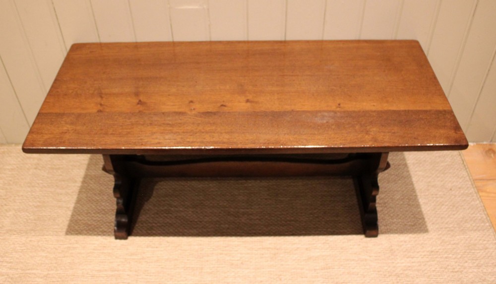 A solid oak rectangular low coffee table featuring a plain plank top set on a trestle base with shaped end supports and a single stretcher rail. View XI