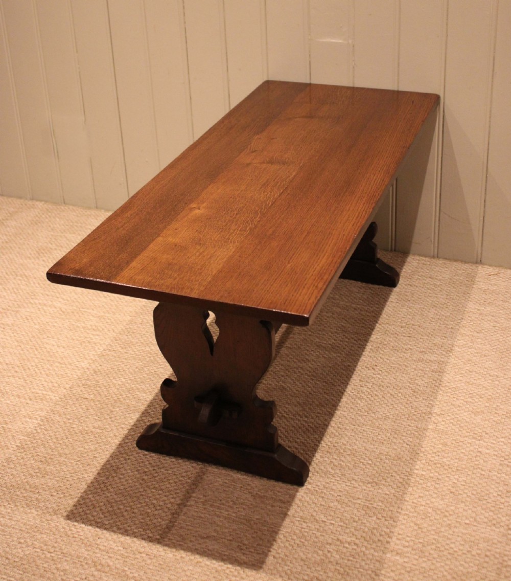 A solid oak rectangular low coffee table featuring a plain plank top set on a trestle base with shaped end supports and a single stretcher rail. View XII