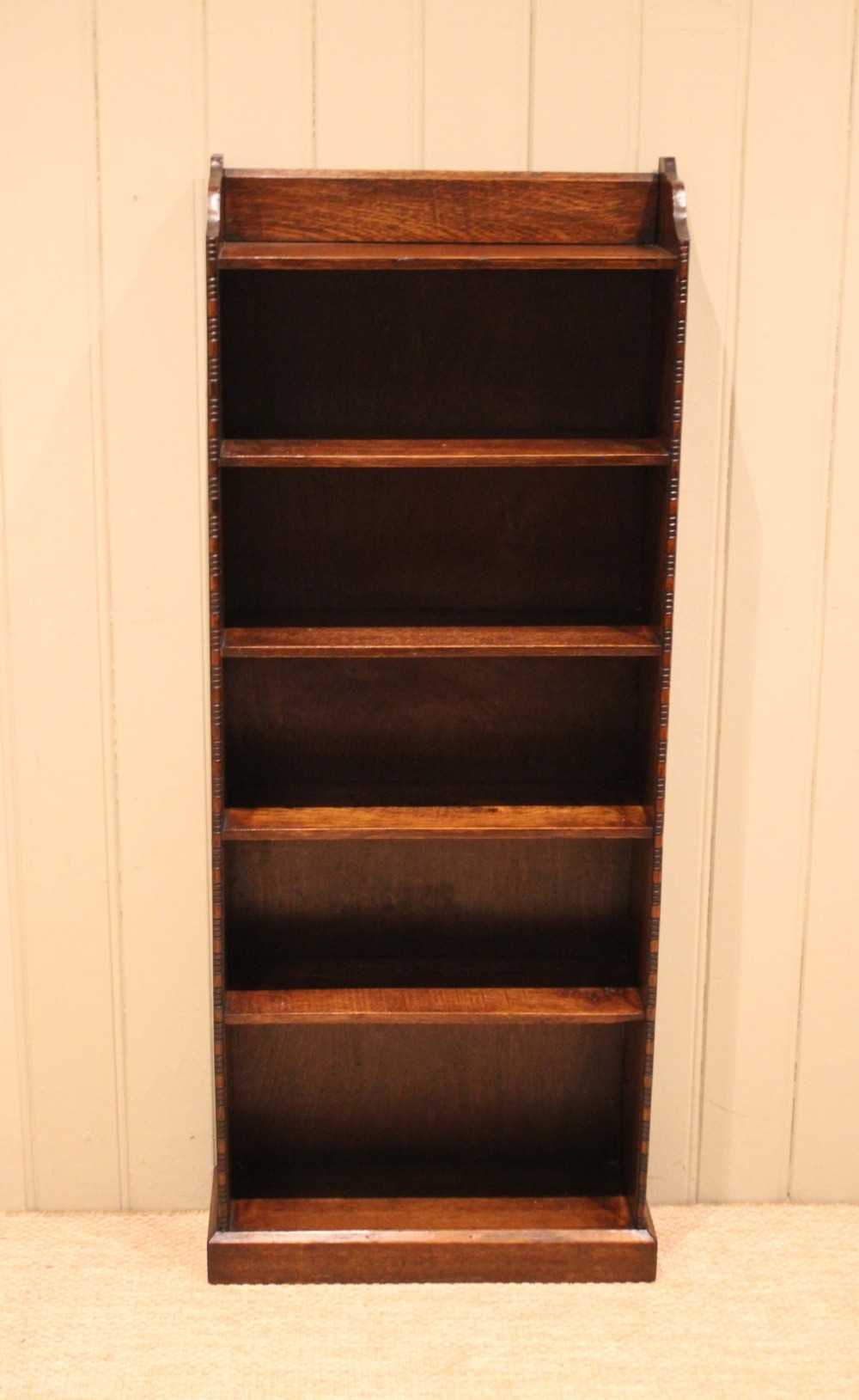 A tall, narrow dark oak open bookcase featuring five fixed shelves filled with vintage hardback books and a simple gallery top on a plinth base. View II