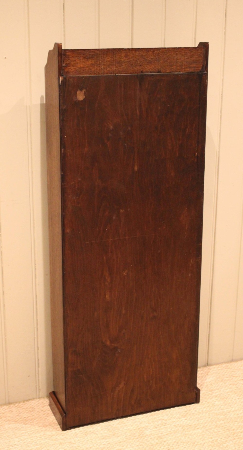 A tall, narrow dark oak open bookcase featuring five fixed shelves filled with vintage hardback books and a simple gallery top on a plinth base. View XII