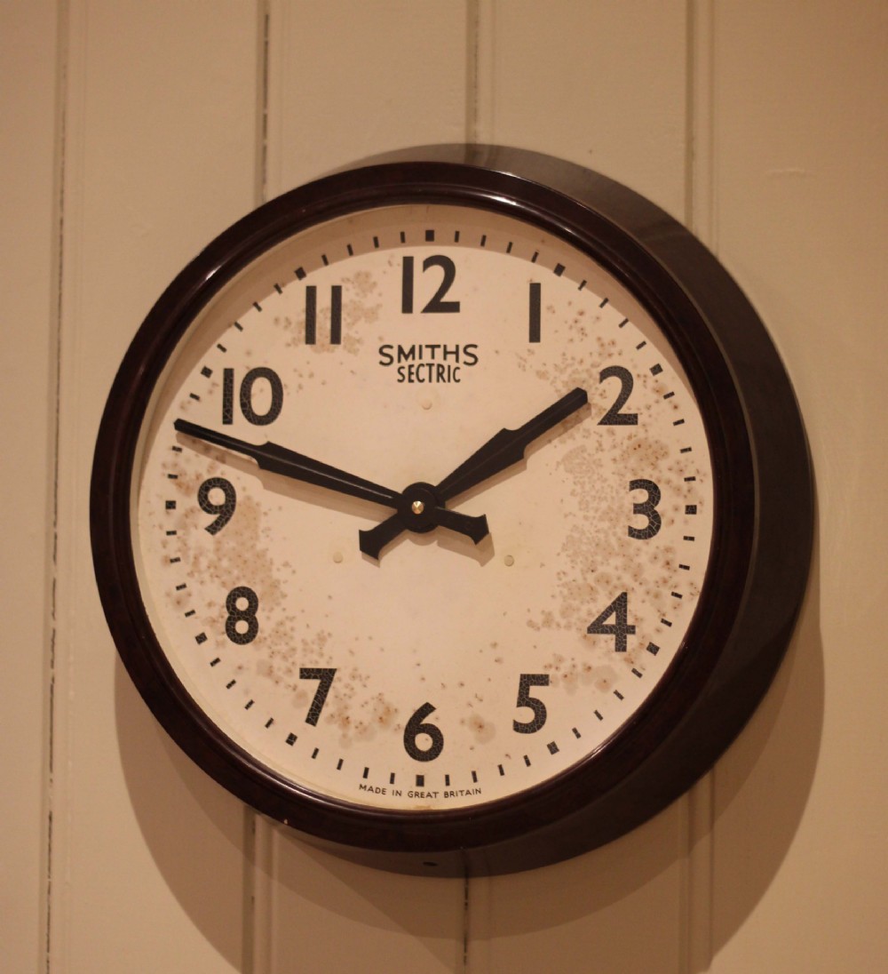 A circular vintage British Smiths Sectric wall clock featuring a dark brown Bakelite frame and an off-white dial with black Arabic numerals. View II