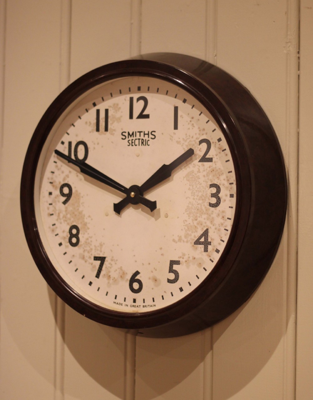A circular vintage British Smiths Sectric wall clock featuring a dark brown Bakelite frame and an off-white dial with black Arabic numerals. View IV