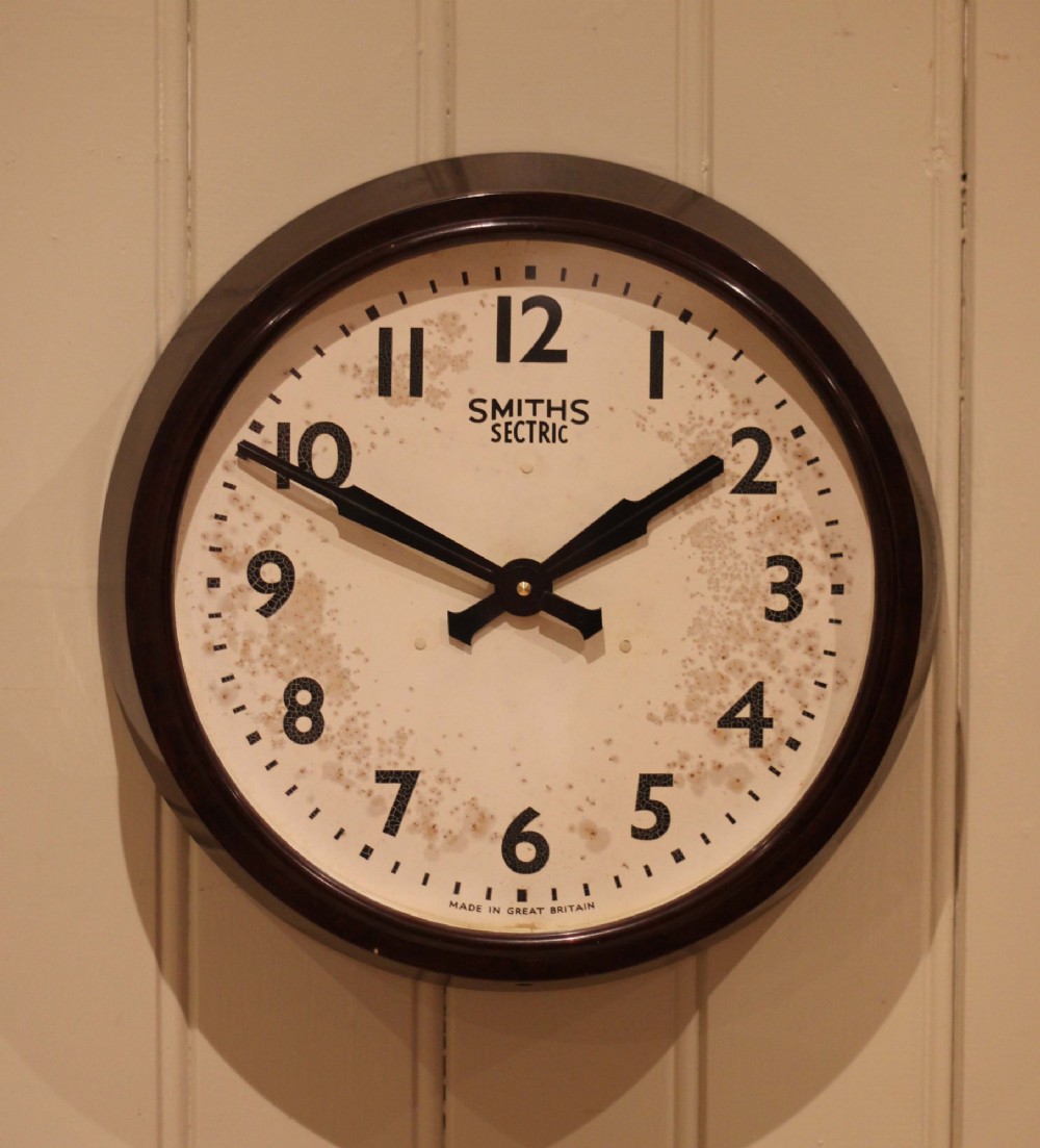 A circular vintage British Smiths Sectric wall clock featuring a dark brown Bakelite frame and an off-white dial with black Arabic numerals. View VI
