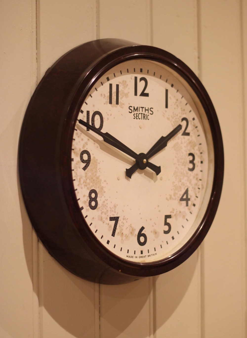 A circular vintage British Smiths Sectric wall clock featuring a dark brown Bakelite frame and an off-white dial with black Arabic numerals. View VIII
