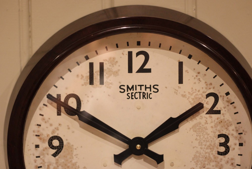 A circular vintage British Smiths Sectric wall clock featuring a dark brown Bakelite frame and an off-white dial with black Arabic numerals. View IX