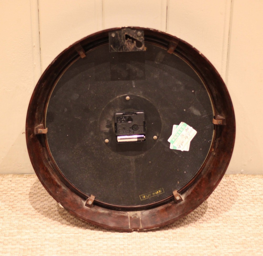A circular vintage British Smiths Sectric wall clock featuring a dark brown Bakelite frame and an off-white dial with black Arabic numerals. View X