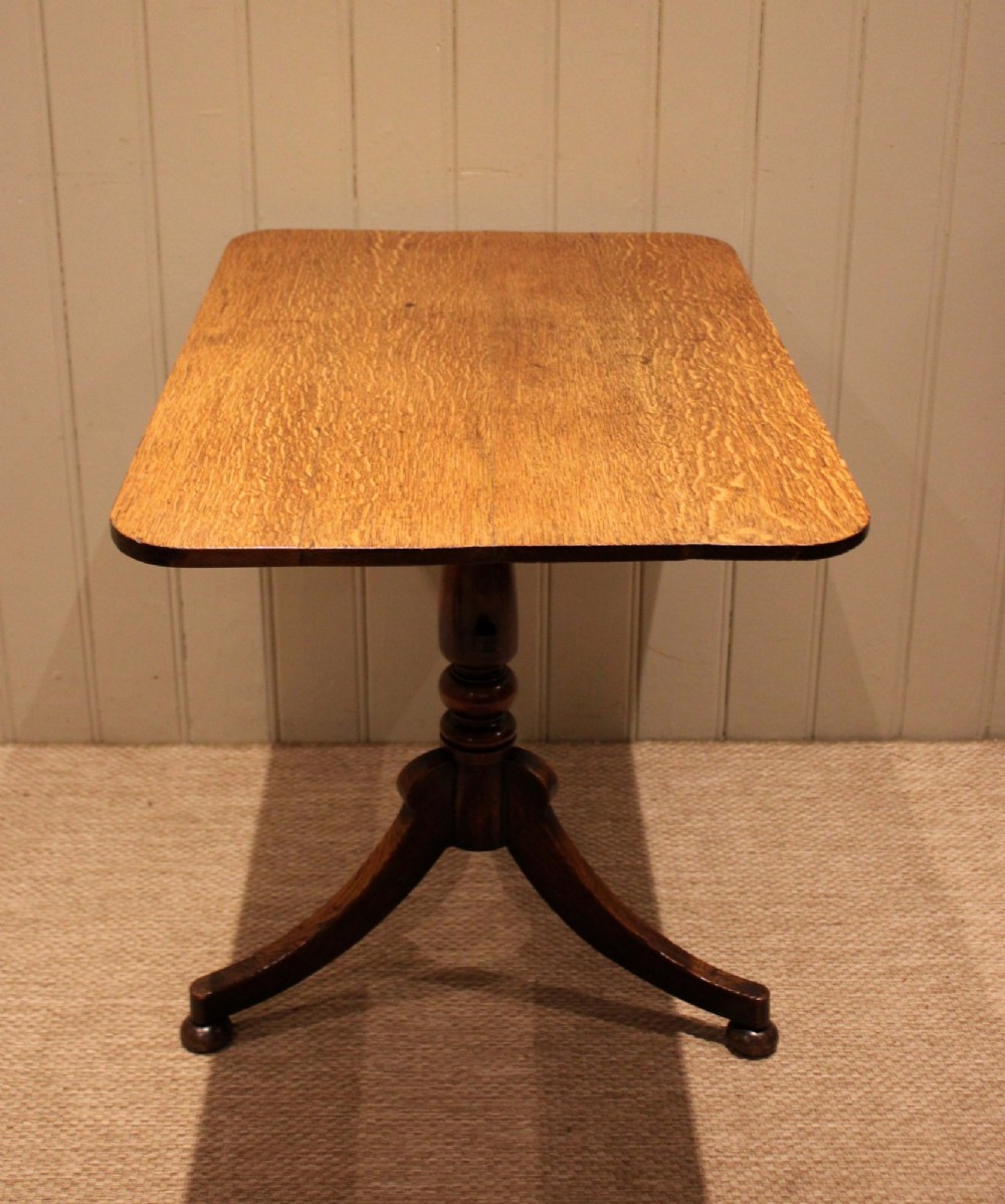 A late Georgian oak tilt-top table featuring a rectangular top with rounded corners, supported by a turned central column and a tripod base.