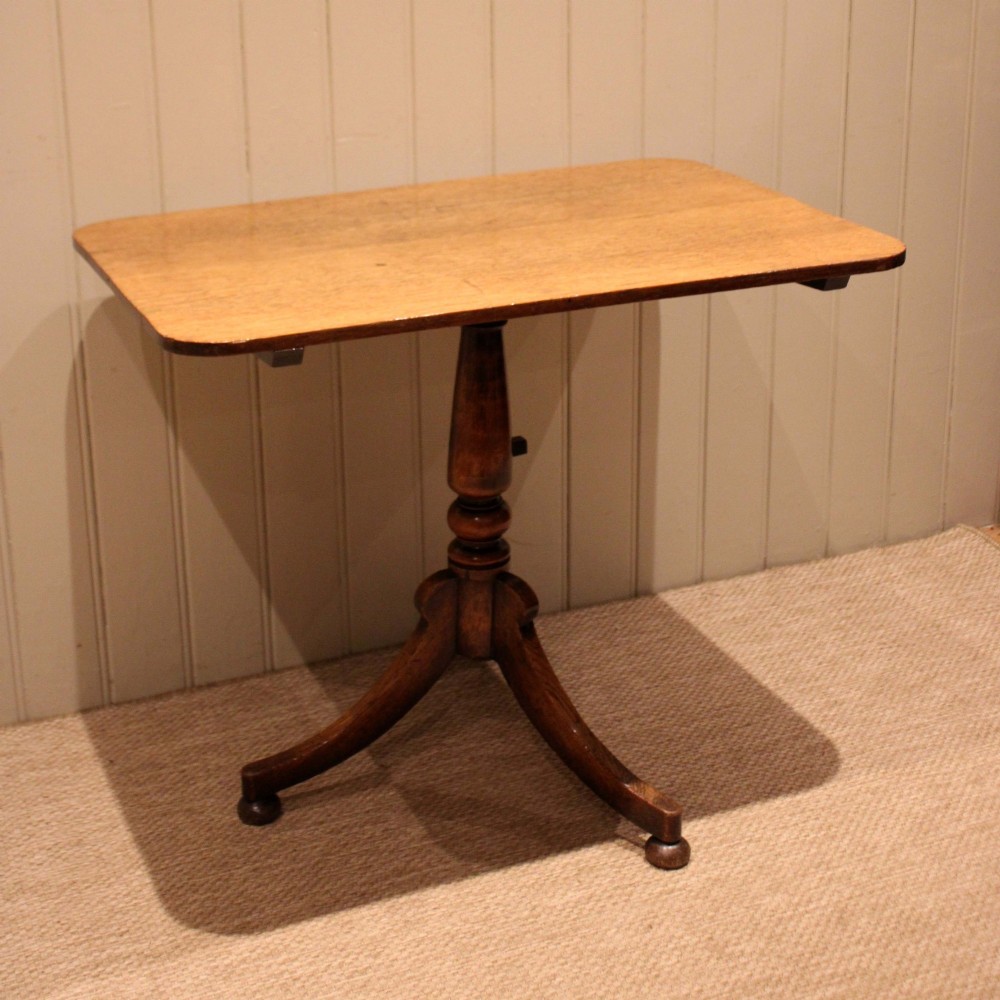 A late Georgian oak tilt-top table featuring a rectangular top with rounded corners, supported by a turned central column and a tripod base. View VII