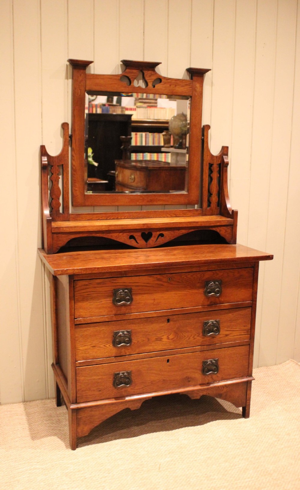 A solid oak Arts and Crafts dressing chest featuring three wide drawers, metal drop handles, heart-shaped cutouts, and a tilting rectangular mirror on top. View VII